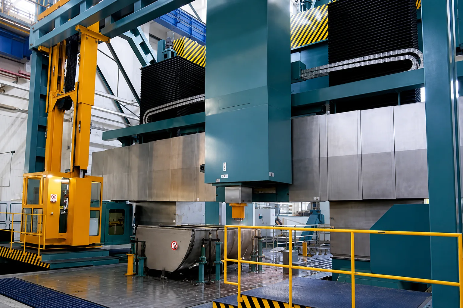 Large gantry milling machine with teal and yellow structure in the workshop