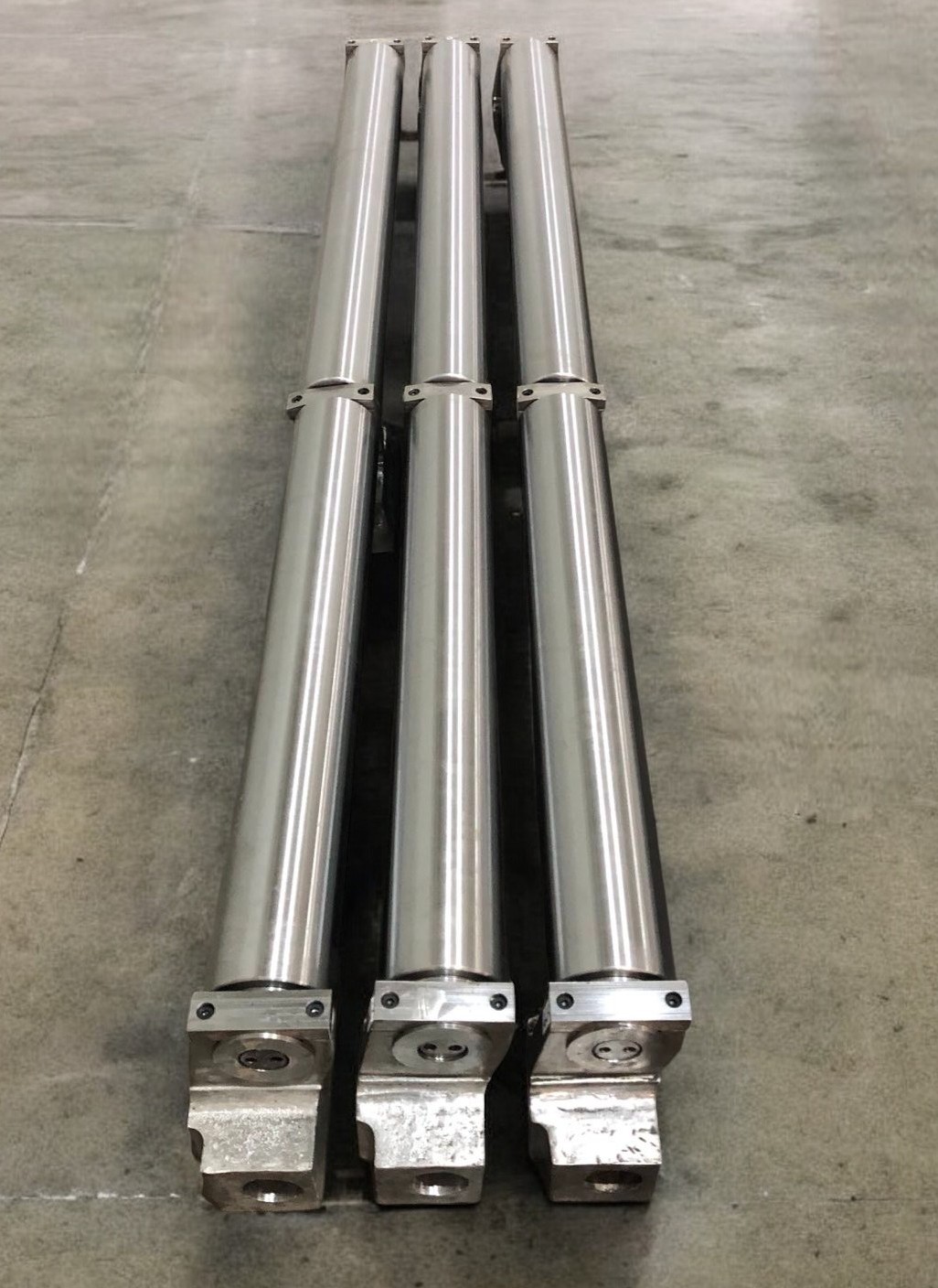 Three long machined rolling mill rolls arranged as a finished set