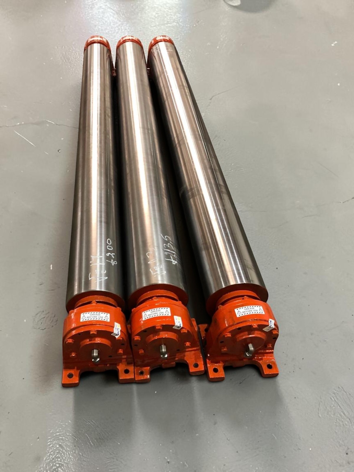 Three polished rolling mill roll assemblies with orange bearing housings