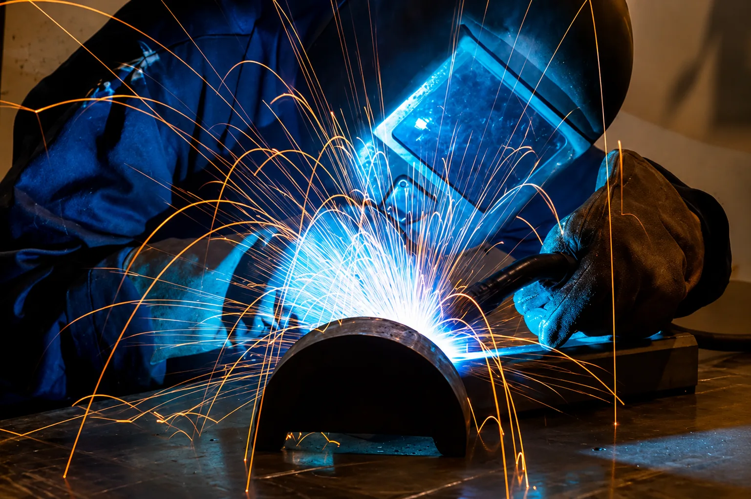 Welder joining a pipe section with bright blue arc light and sparks