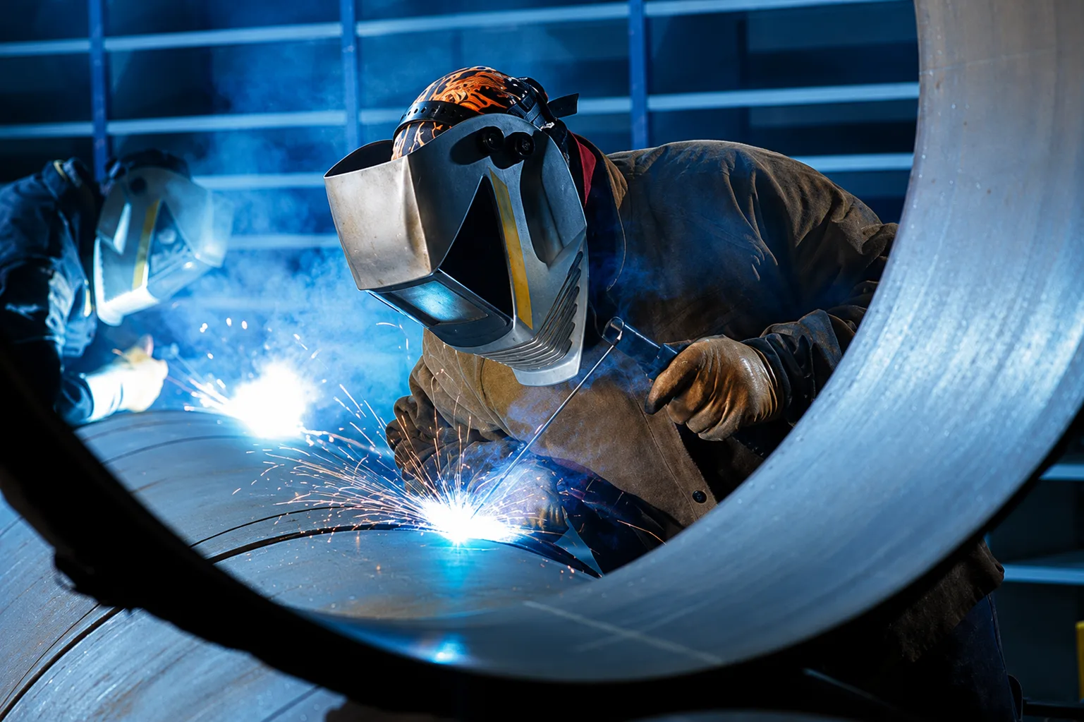 Welders working inside a large circular industrial component with blue arc light
